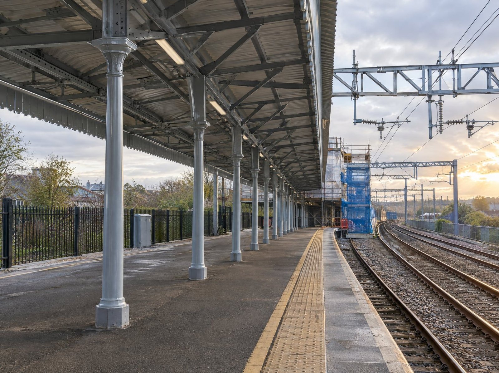 Railway station platform canopy with freshly repainted steel columns and trusses, and scaffolding beyond