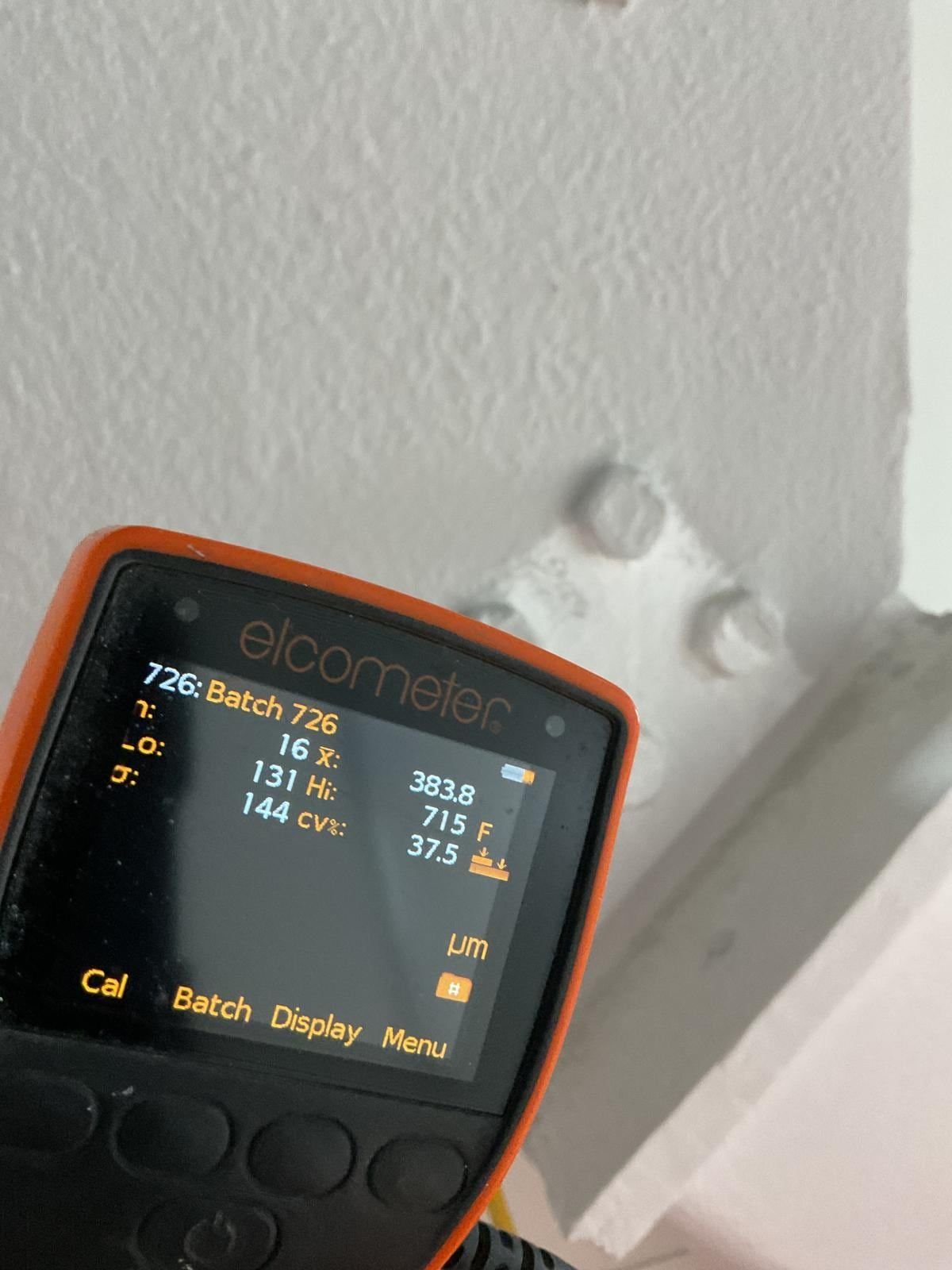 Elcometer coating thickness gauge held beside a white painted bolted steel connection