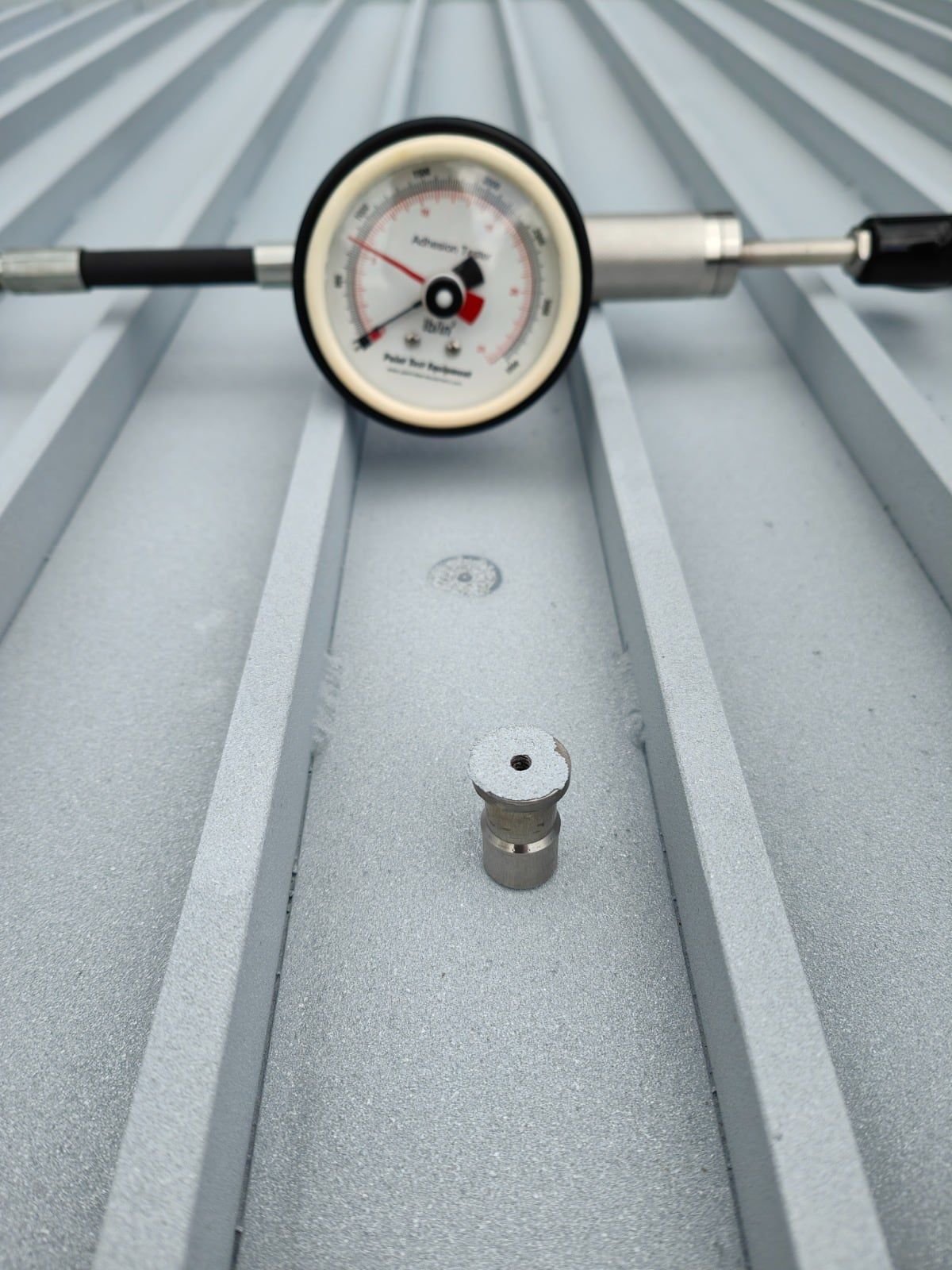Pull-off adhesion tester and a test dolly on a coated profiled metal roof