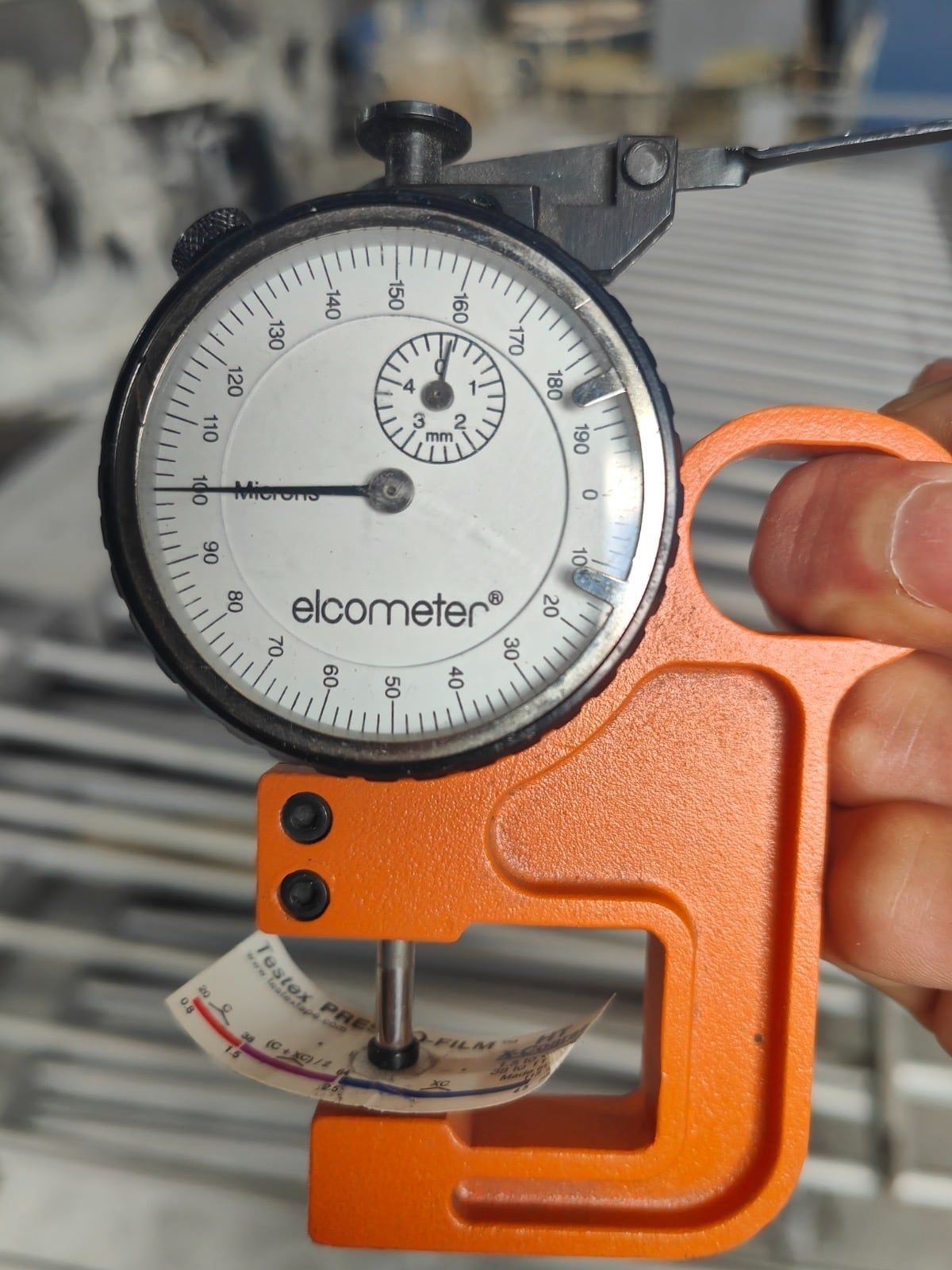 Dial micrometer measuring a strip of replica tape to find the surface profile of blasted steel
