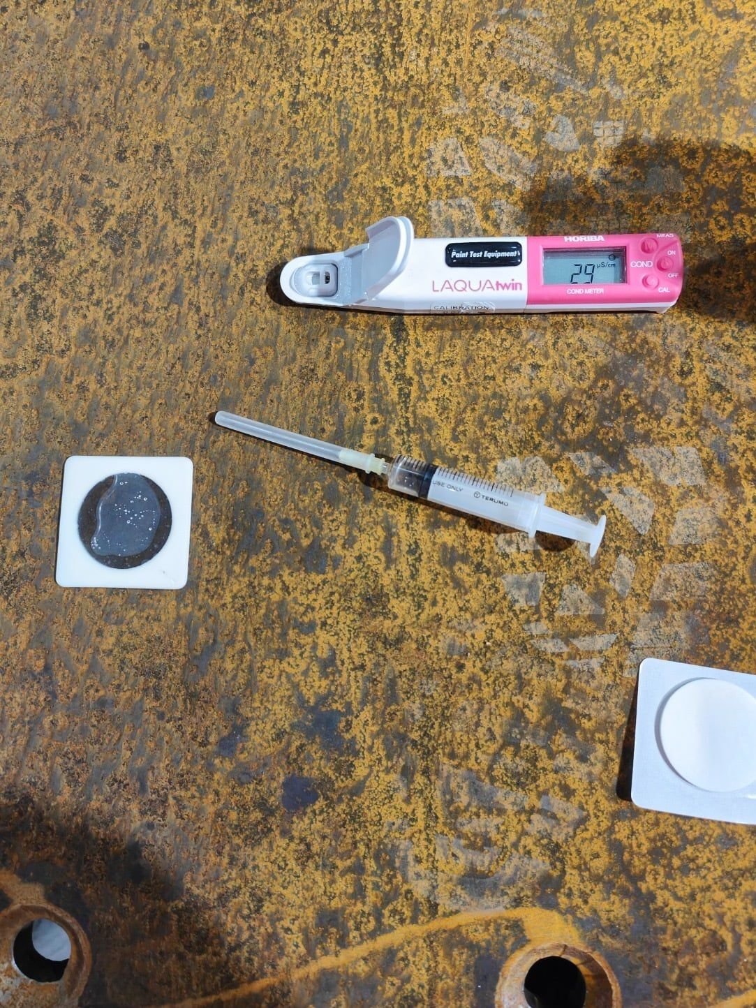 Soluble salt test on rusty steel: a Bresle patch, a syringe and a conductivity meter reading 29 microsiemens per centimetre